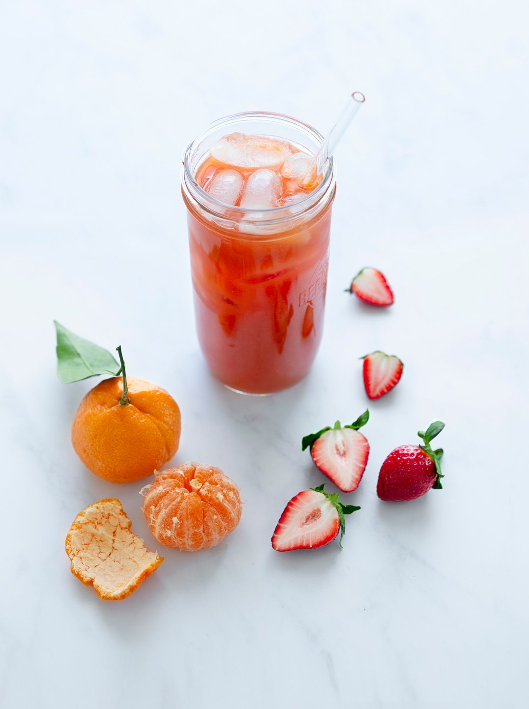 a jar filled with carrot papaya juice over ice with a mandarin and strberries