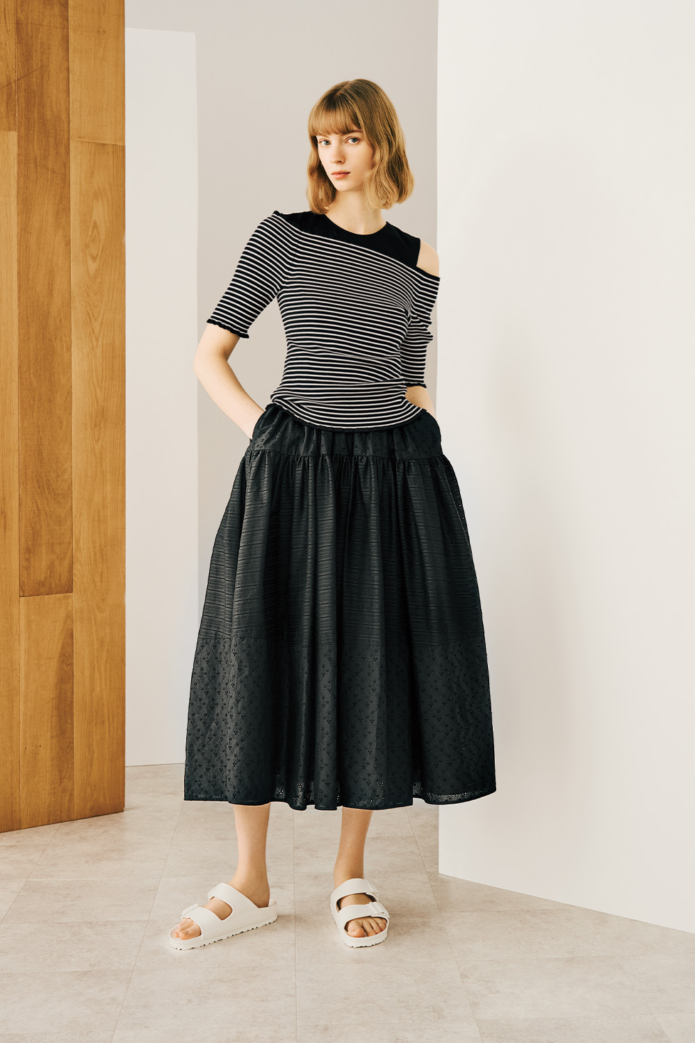 A woman is wearing a black striped pattern top paired with a black skirt stands