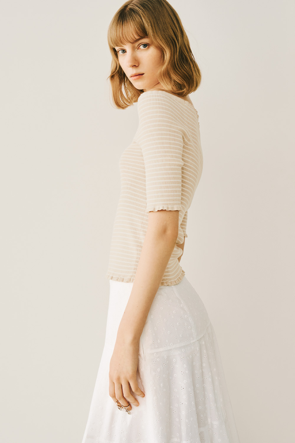 A model is dressed in a white skirt and a beige top