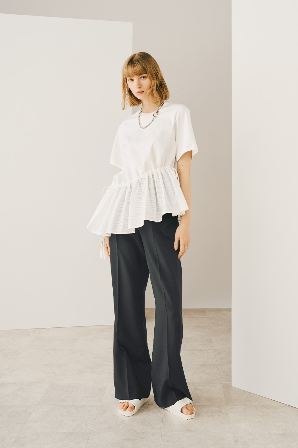 A model is wearing a white top and dark gray wide-legged pants