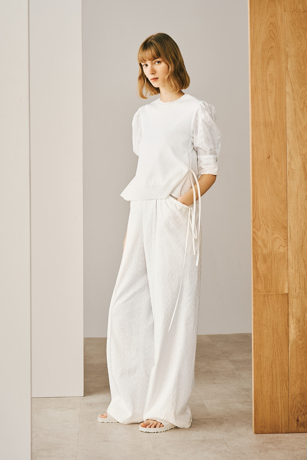A model is wearing a white blouse paired with wide pants