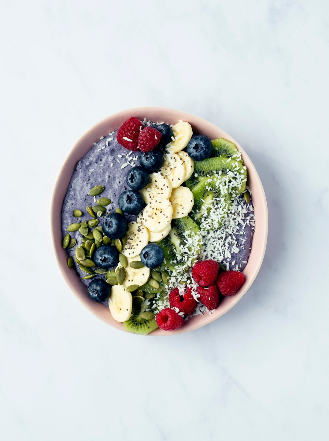 a blueberry cardamom chia bowl topped with berries banana kiwi and shredded coconut