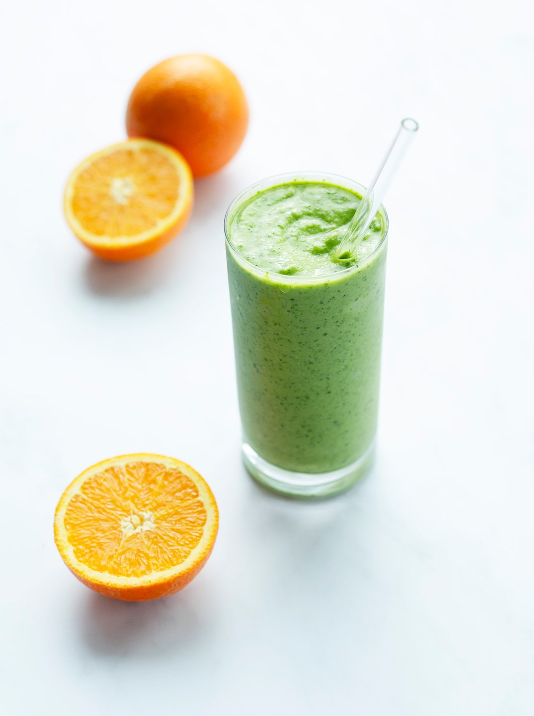 oranges on a counter with a tall glass of green citrus smoothie