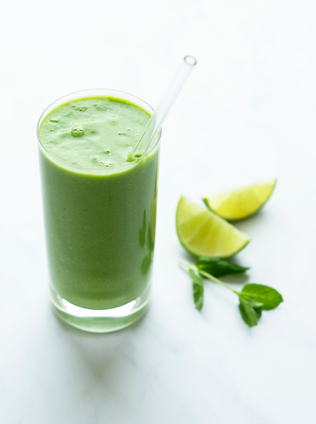 A glass of all green smoothie with lime wedges and mint on the side
