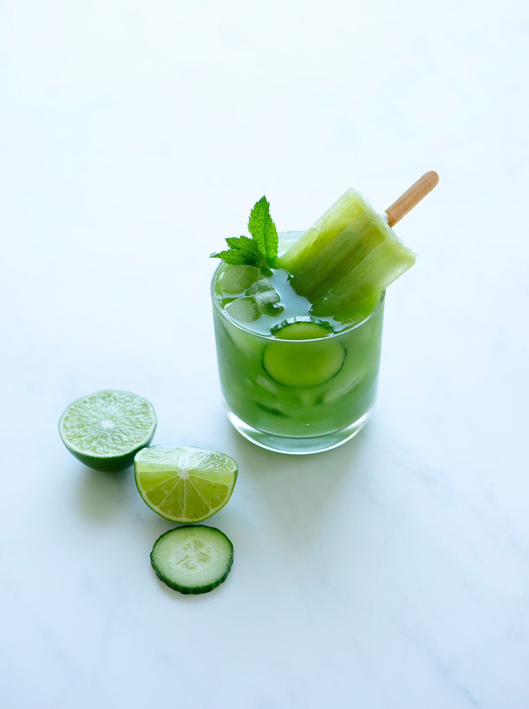 a glass of juice with a Cucumber Mint + Lime Popsicle 