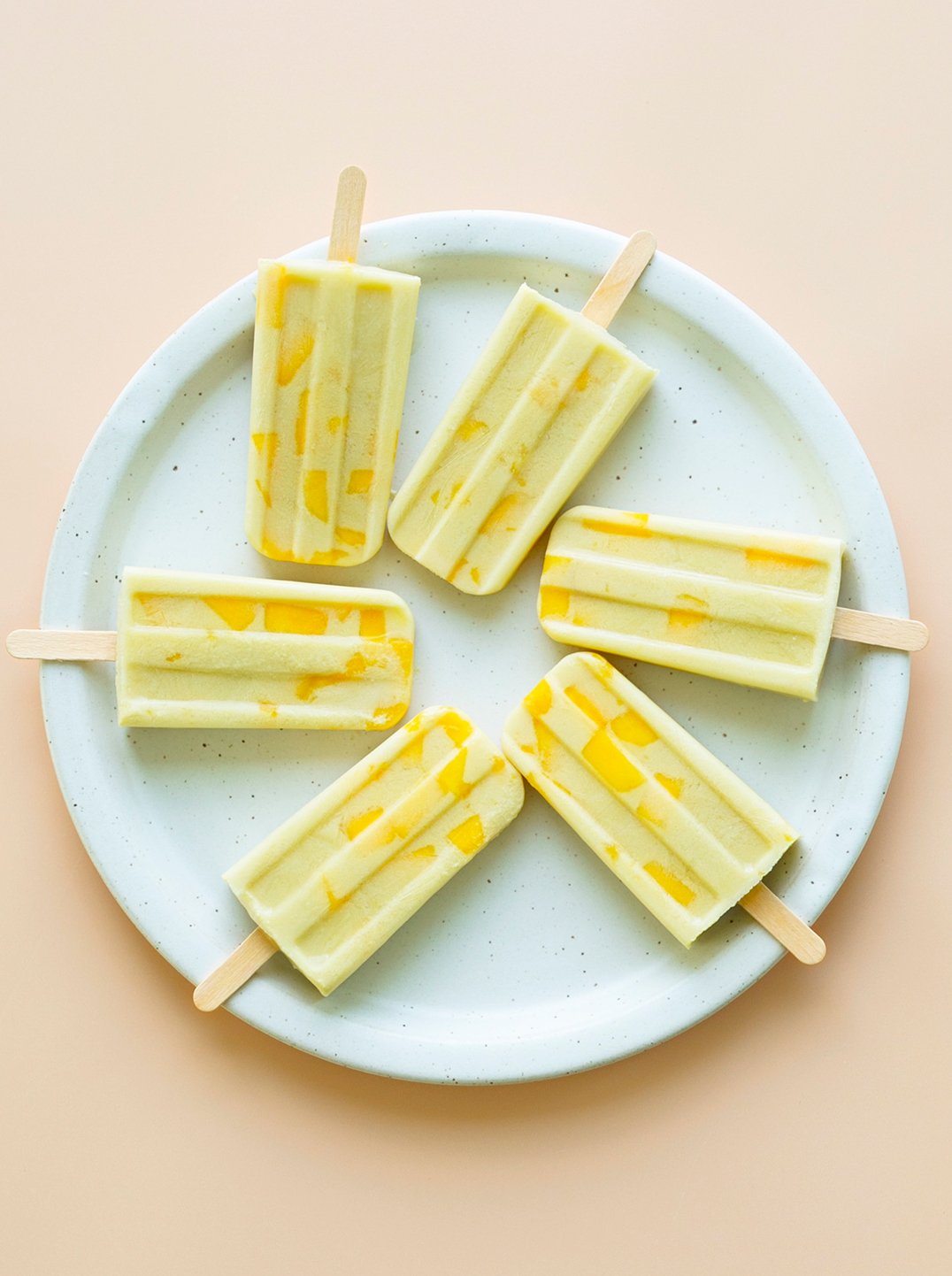 6 Mango Coconut Popsicles on a pale green plate