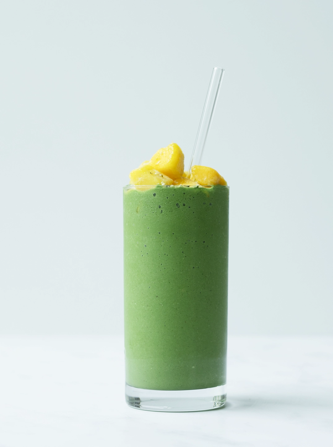 a tall glass og green mango recovery smoothie topped with mango pieces
