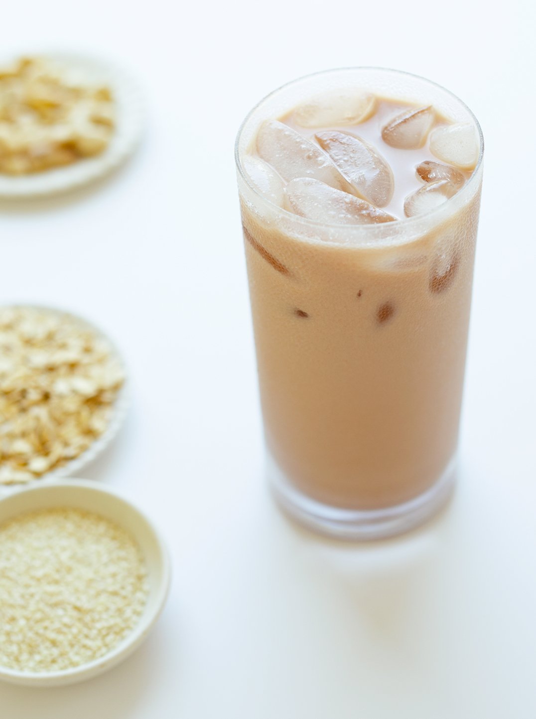 a tall glass of sesame strength milk with ice and 3 small bowls with ingredients