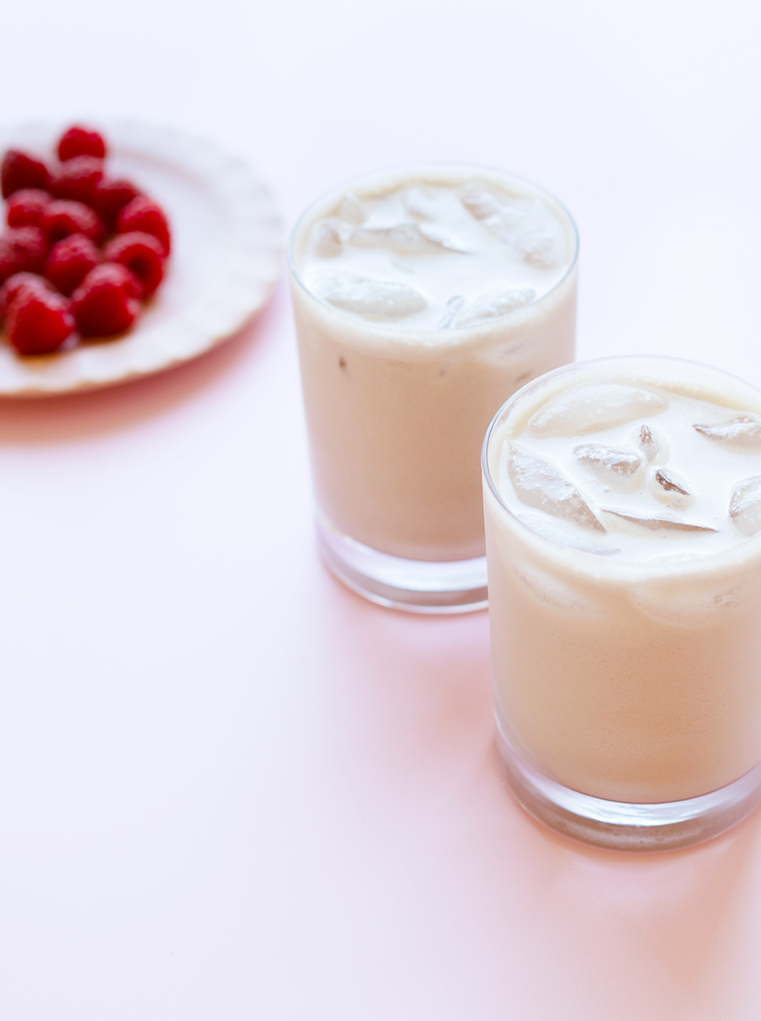 2 glasses of Pistachio & Almond Berry Boost over ice with a plate of raspberries in the background
