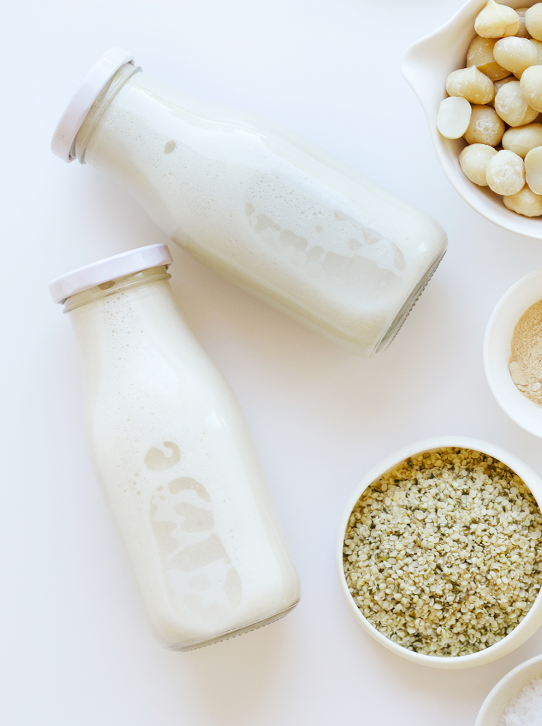 two bottles of maca energy milk with 3 small bowls of ingredients. 
