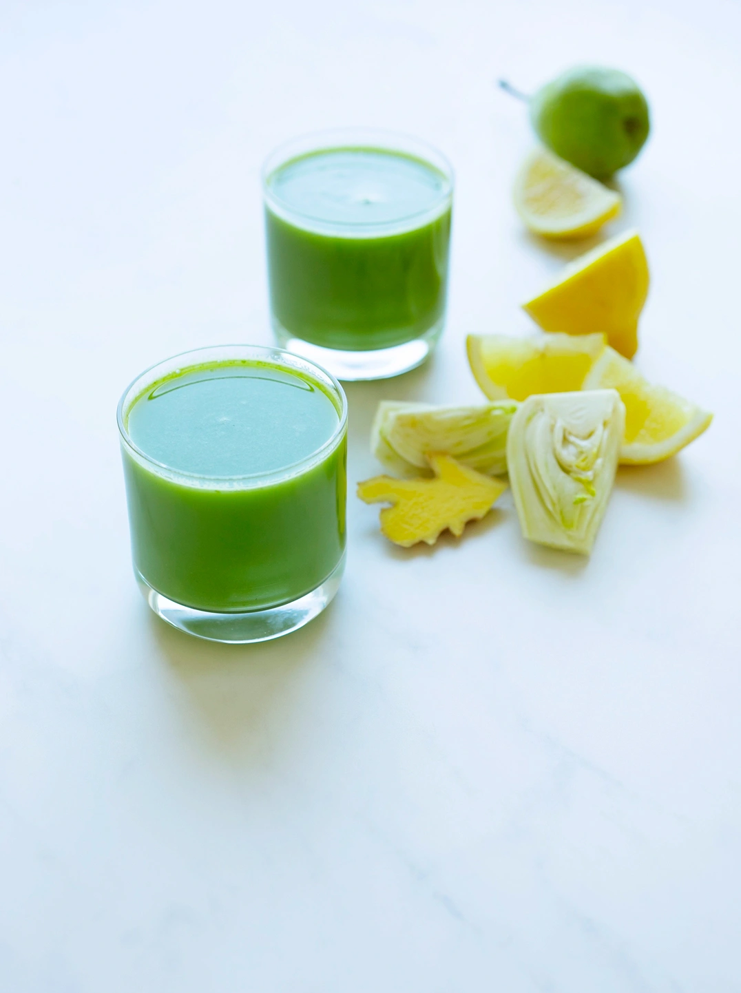 2 glasses of fall reset juice with lemon wedges and a green pear