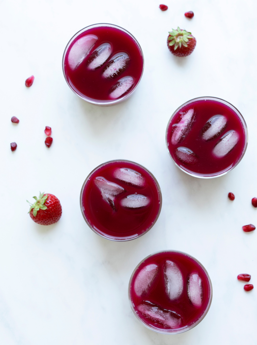 Glasses of deep red juice with ice and a few pomegranate seeds and a strawberry