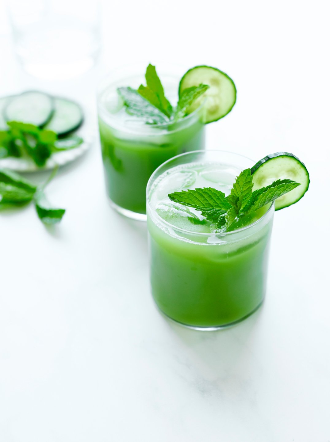Two glasses of bright green juice garnished with cucumber and mint