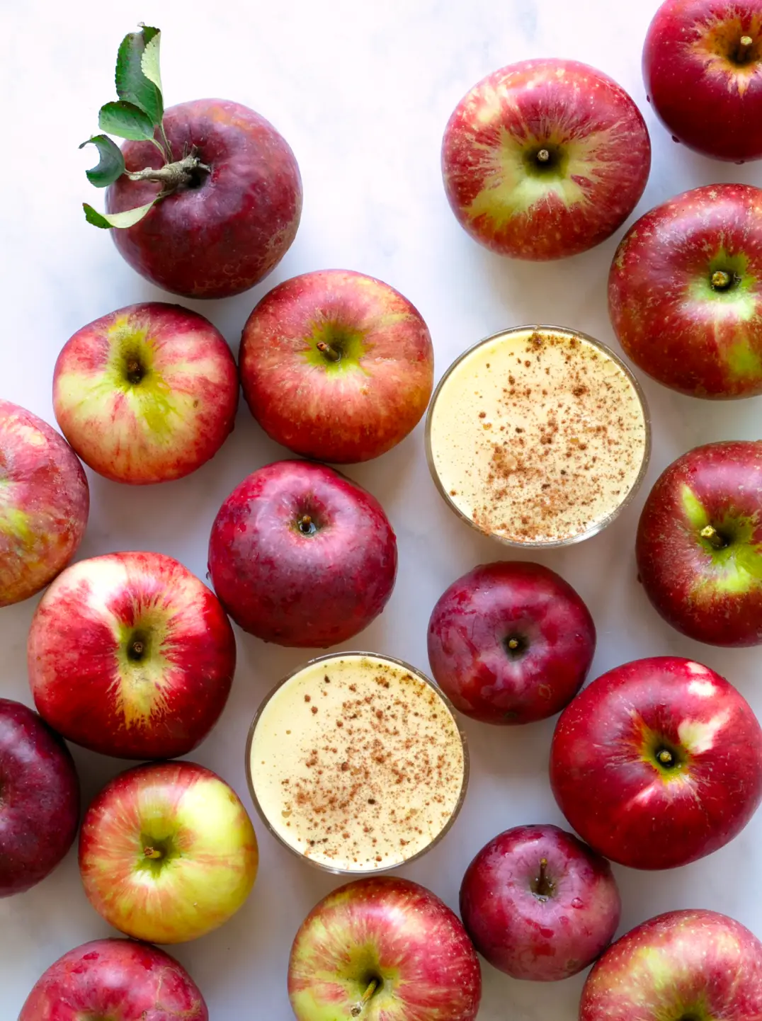red apples surround two glasses of apple chai spice juice