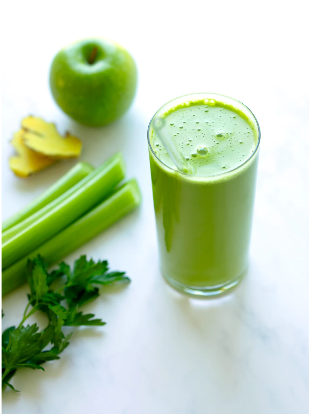 green apples celery and a glass of green apple crisp juice with a glass straw