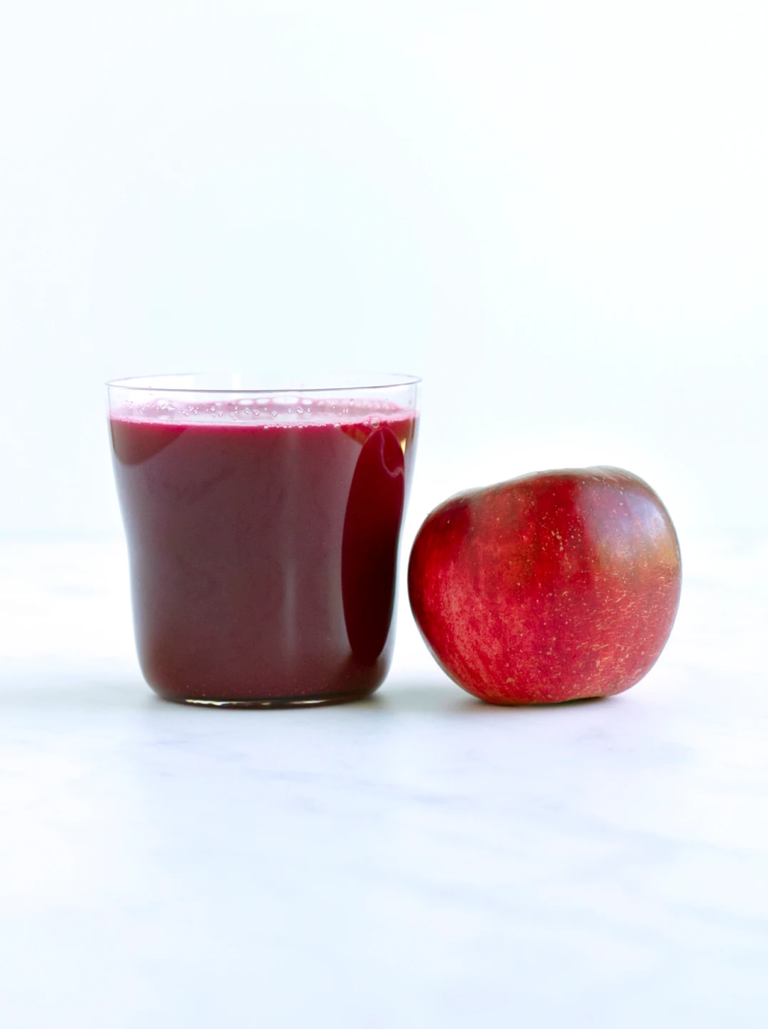 a glass of deep red crimson apple juice with an apple