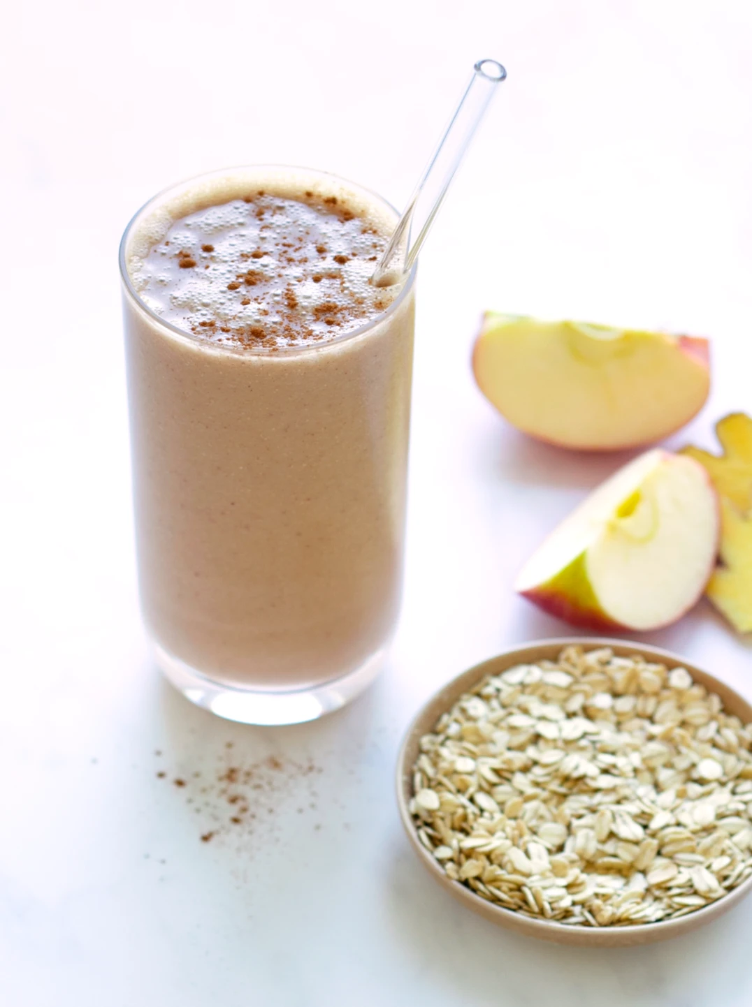 a talll glass of apple pie smoothie, apple pieces and a small bowl of oats