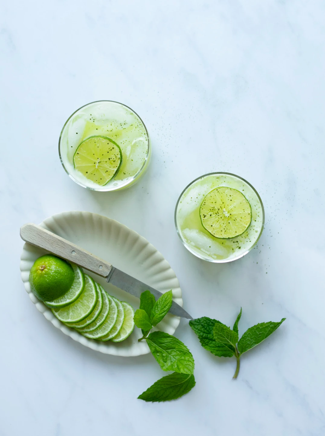 two glasses of green apple mint fizz with ingredients and a knife
