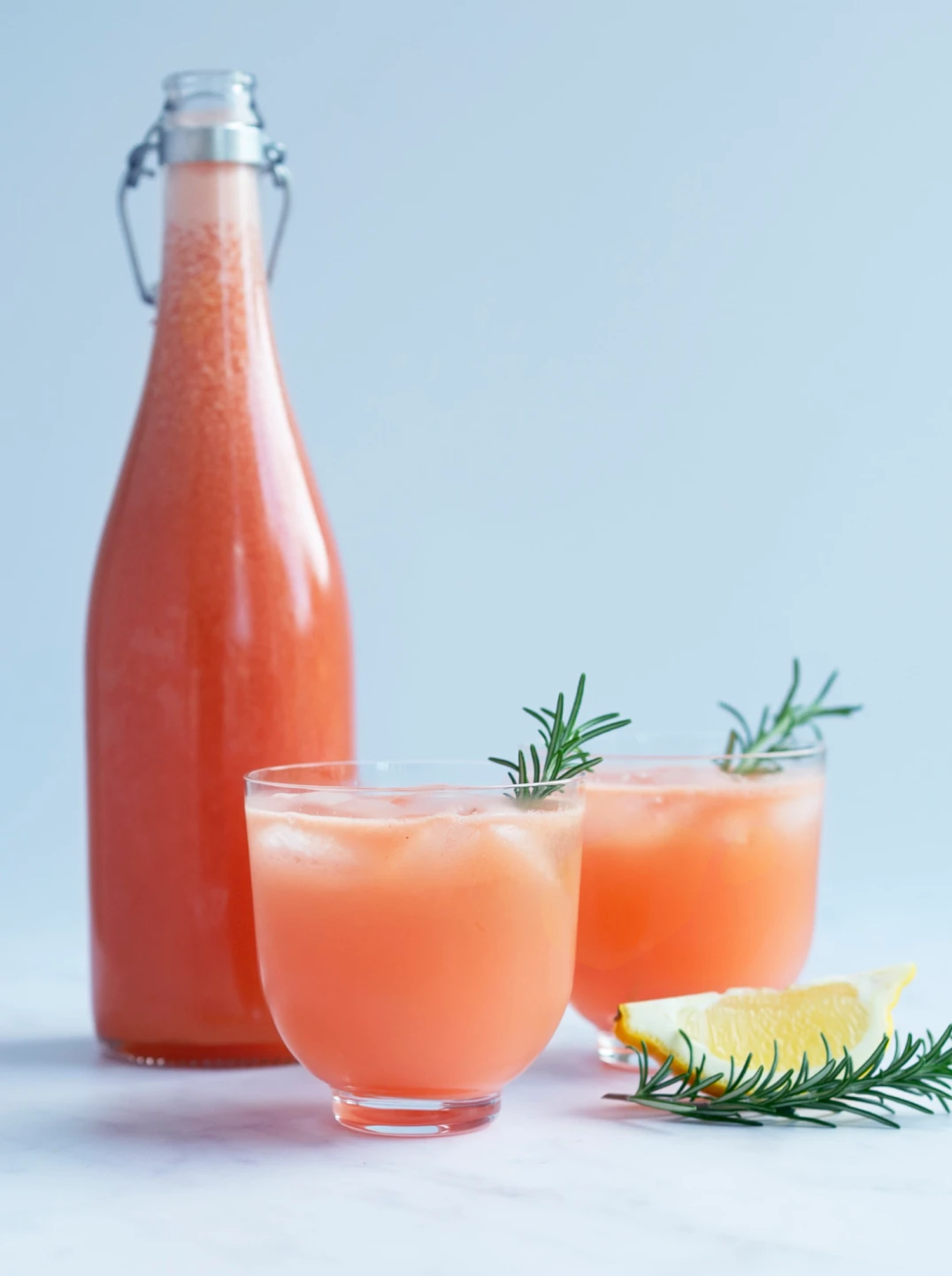 A tall bottle and two glasses filled with ruby red & rosemary spritz
