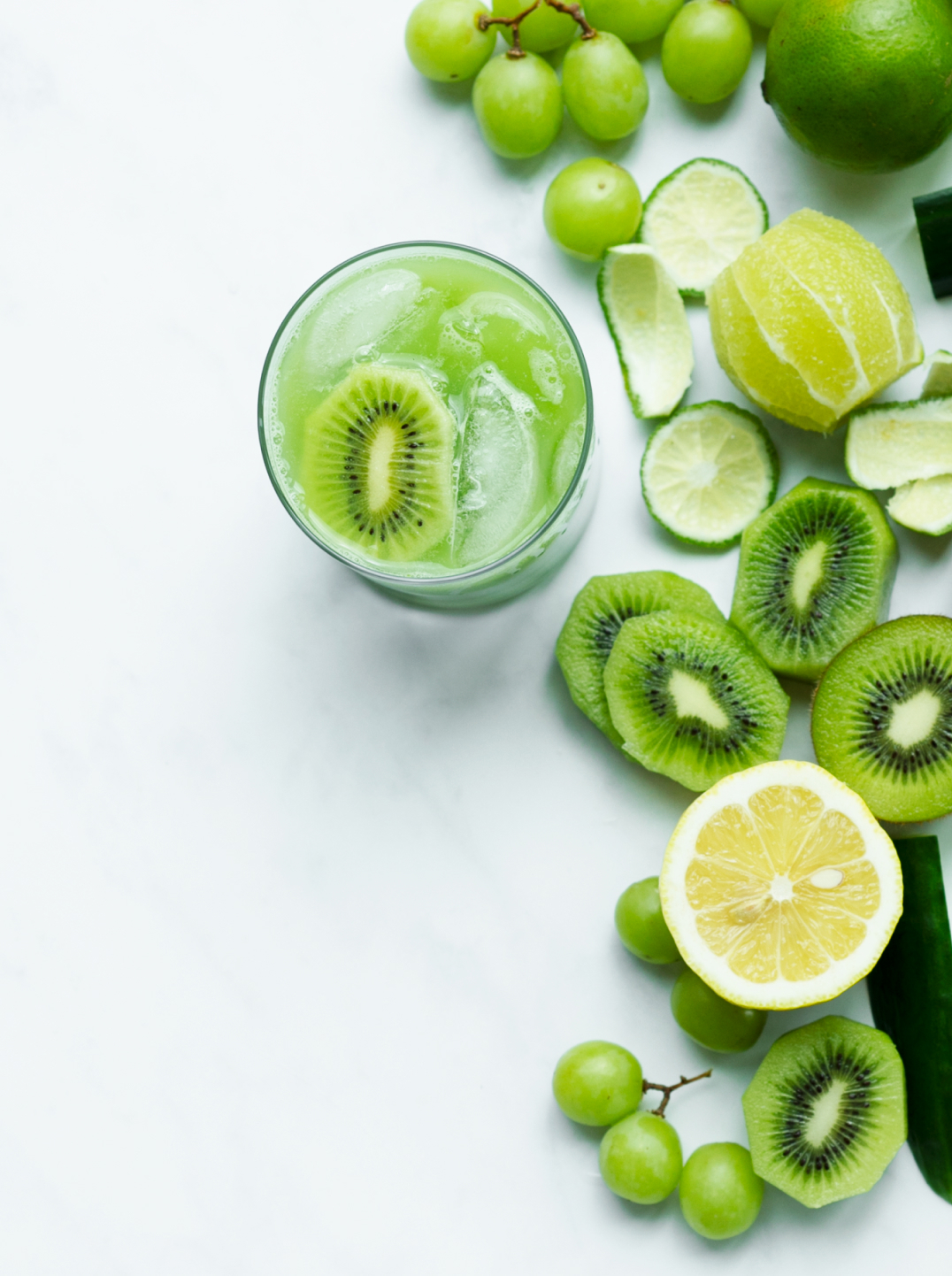 Glass of juice with chopped lime, kiwi, grapes, and cucumber