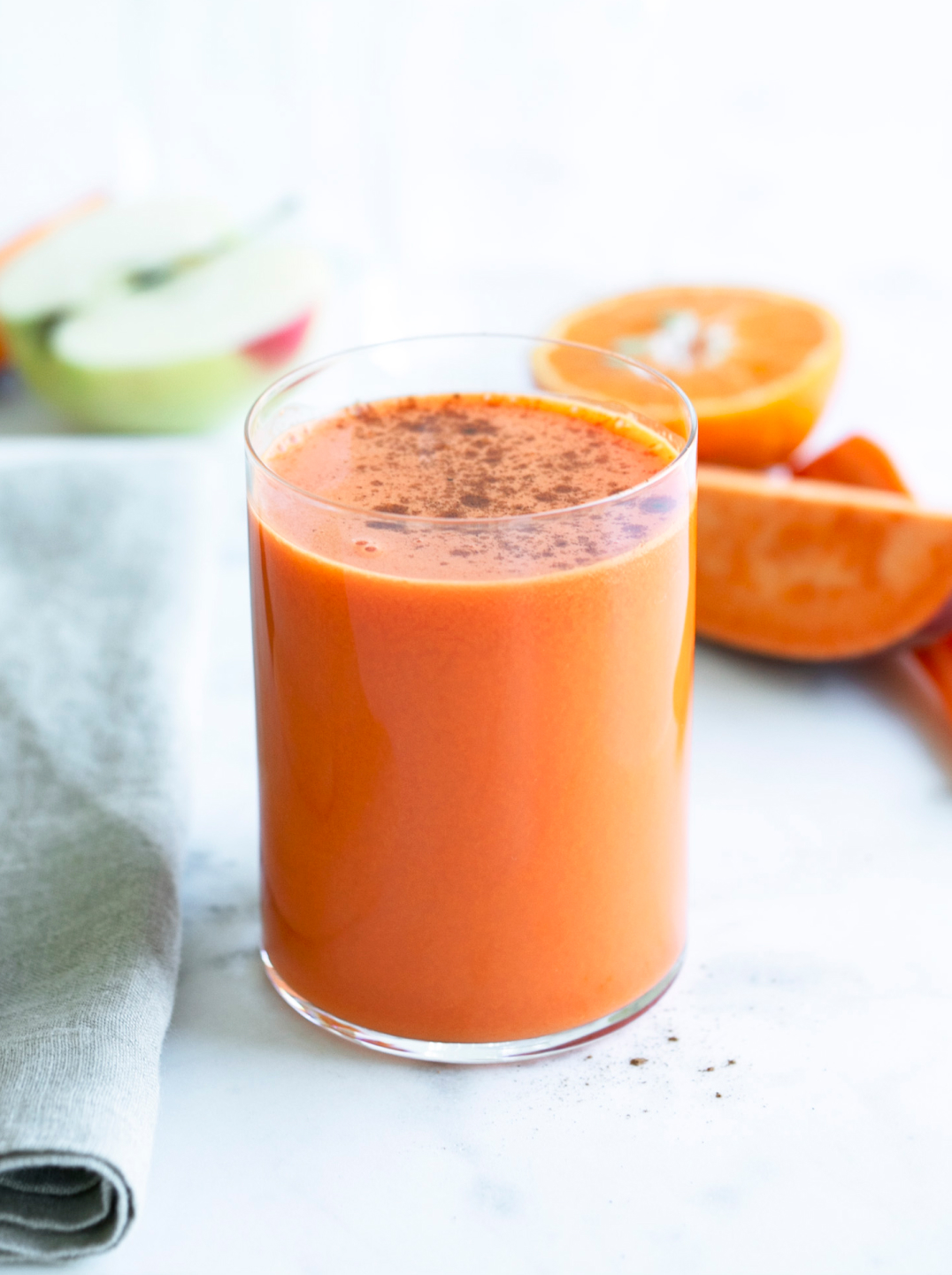 A glass of carrot pumpkin spice juice surrounded by ingredients