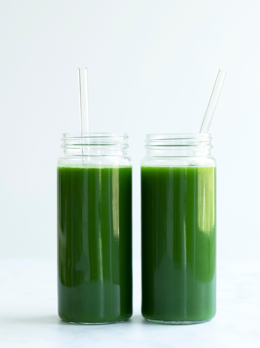 2 Nama glass bottles filled with green harvest juice with a glass straw in each
