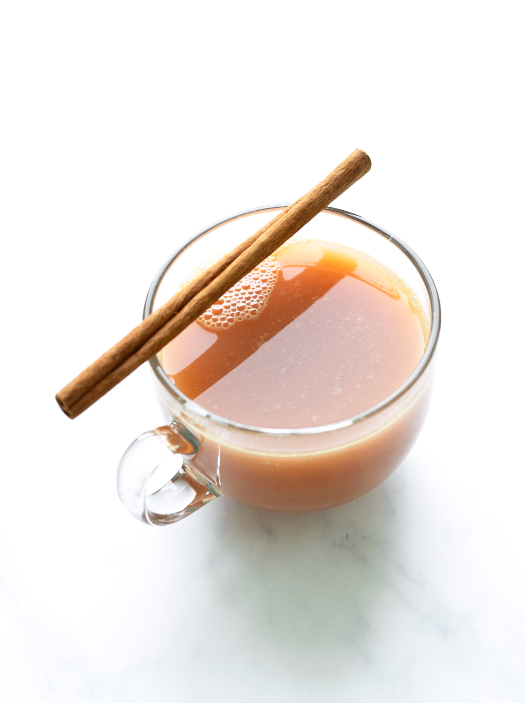 A glass teacup filled with Sweet October Juice and topped with a cinnamon stick