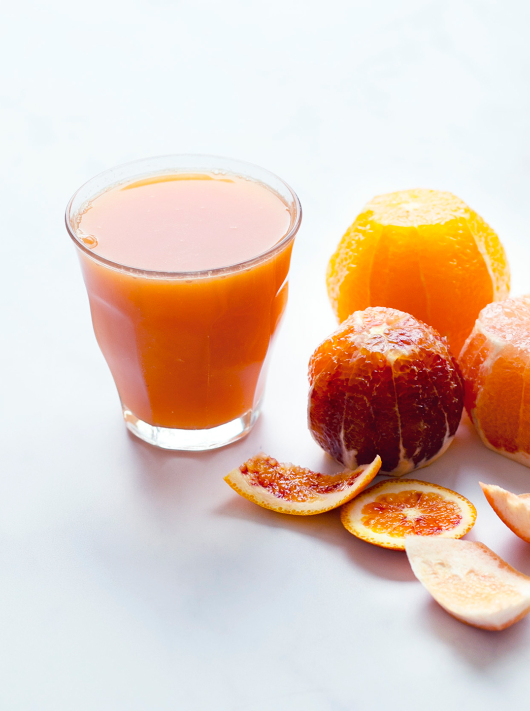 a glass of bright citrus juice with peeled oranges