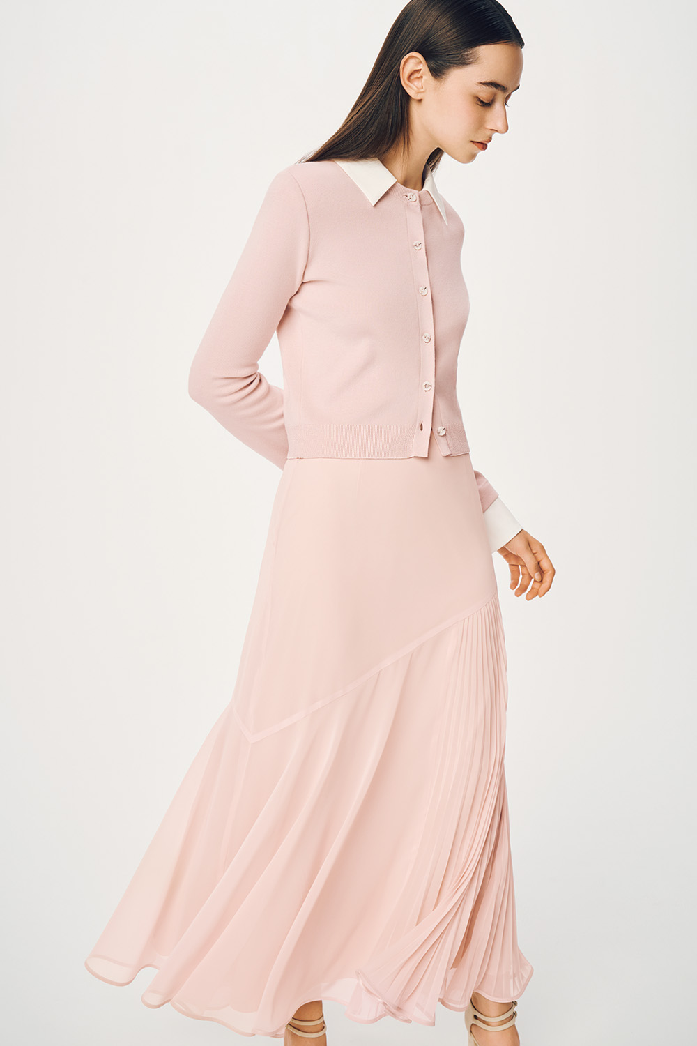 Model is wearing a pink cardigan and a pleated skirt.