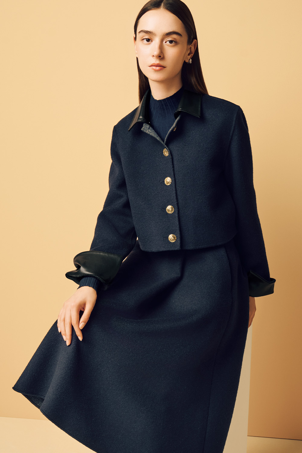 Model is wearing a navy short coat and a skirt.