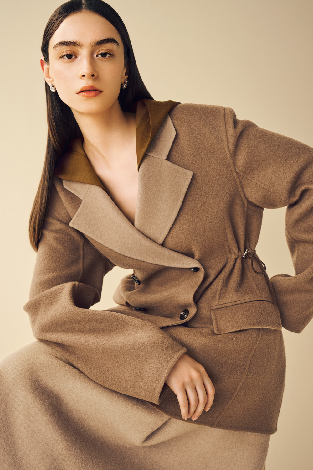 Model is wearing a brown coat on a beige skirt.