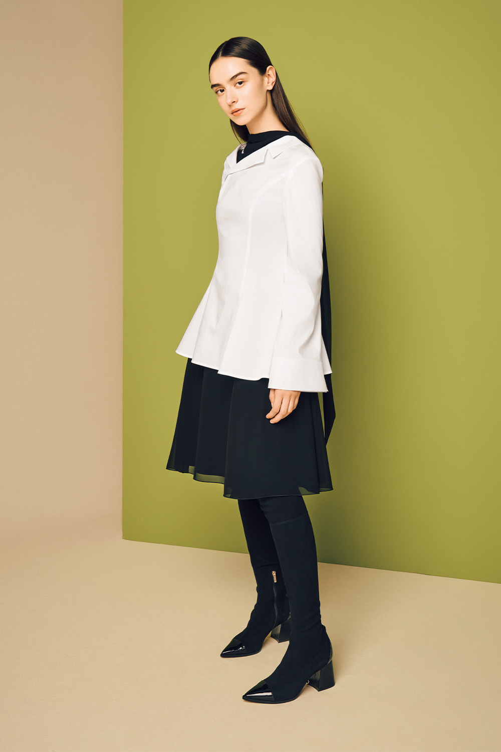 Model is wearing a white top on a black skirt paired with black long boots.