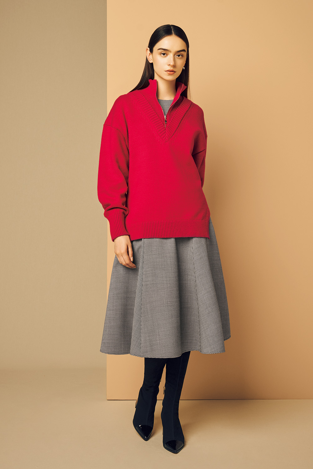 Model is wearing black long boots and a red top on a gray dress.