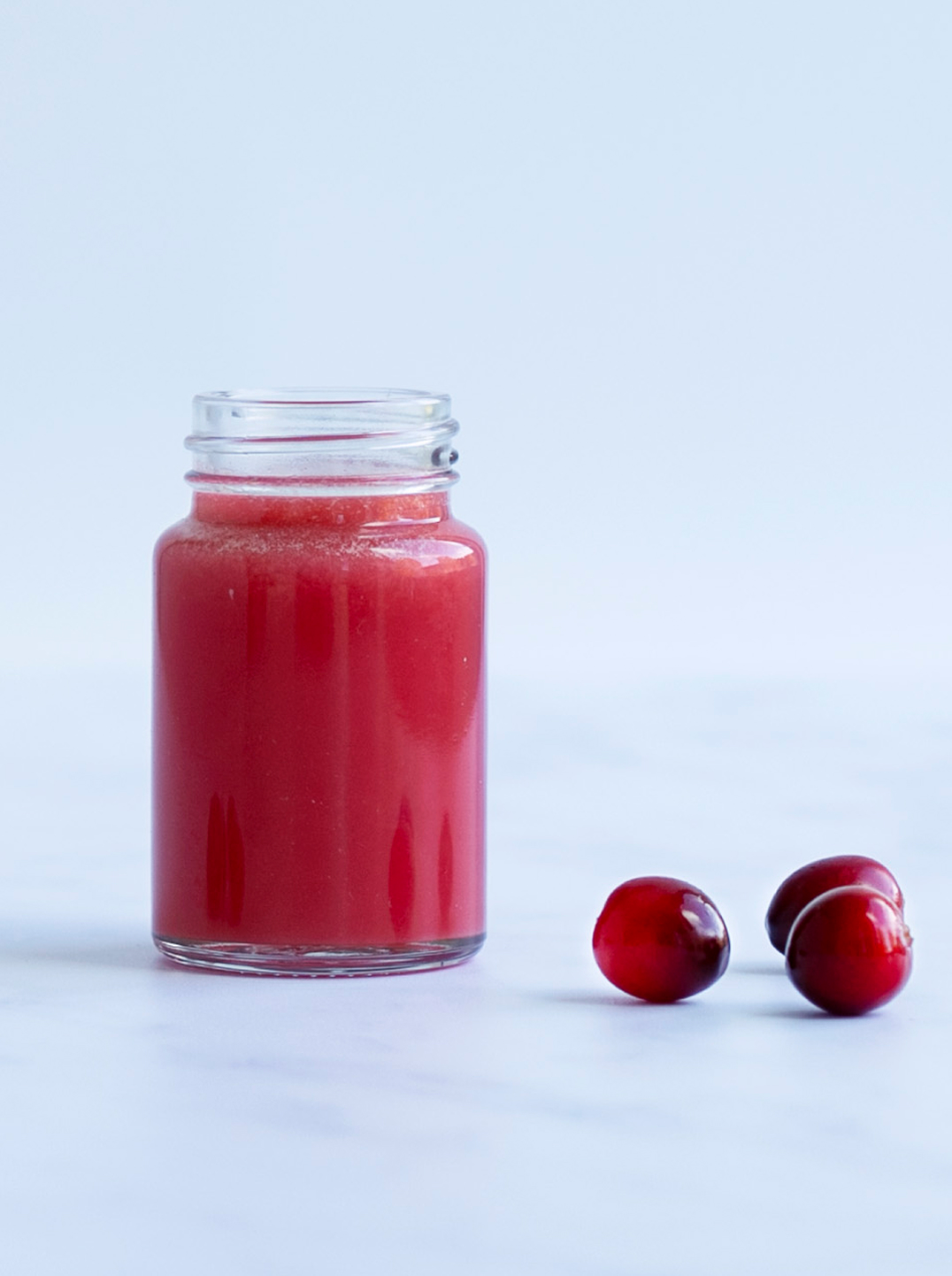 Small bottle of ginger wellness shot with 3 cranberries