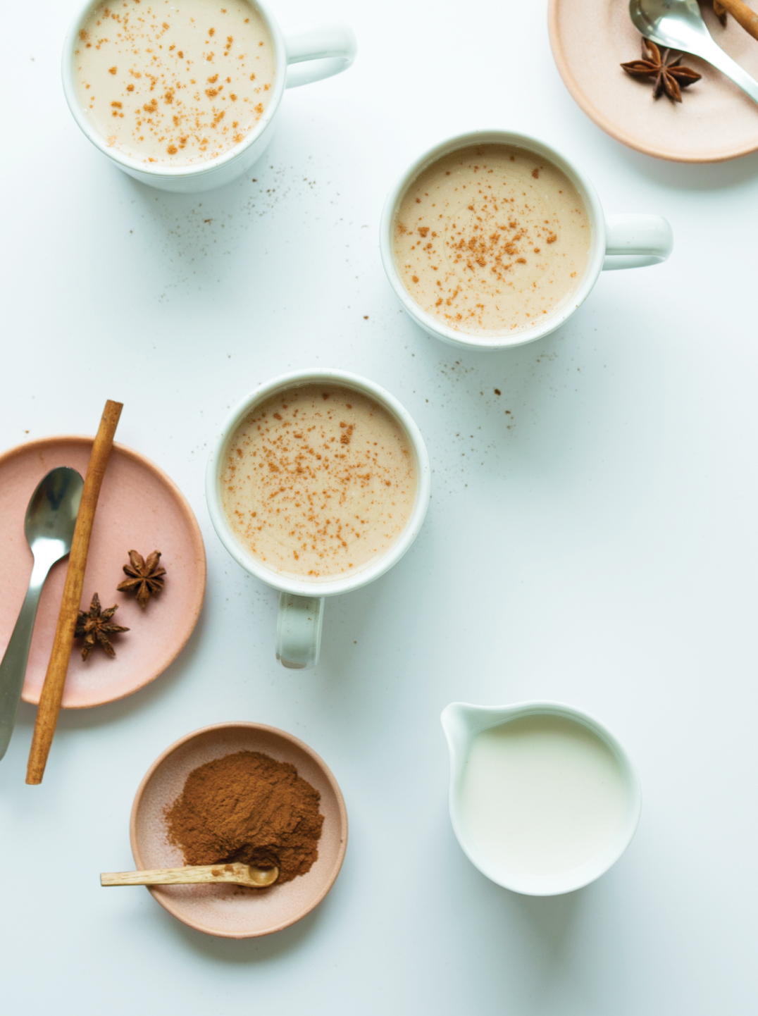 Mugs of coffee topped with Creamy Oat Barista Milk and sprinkled with cinnamon. Small plates with spices