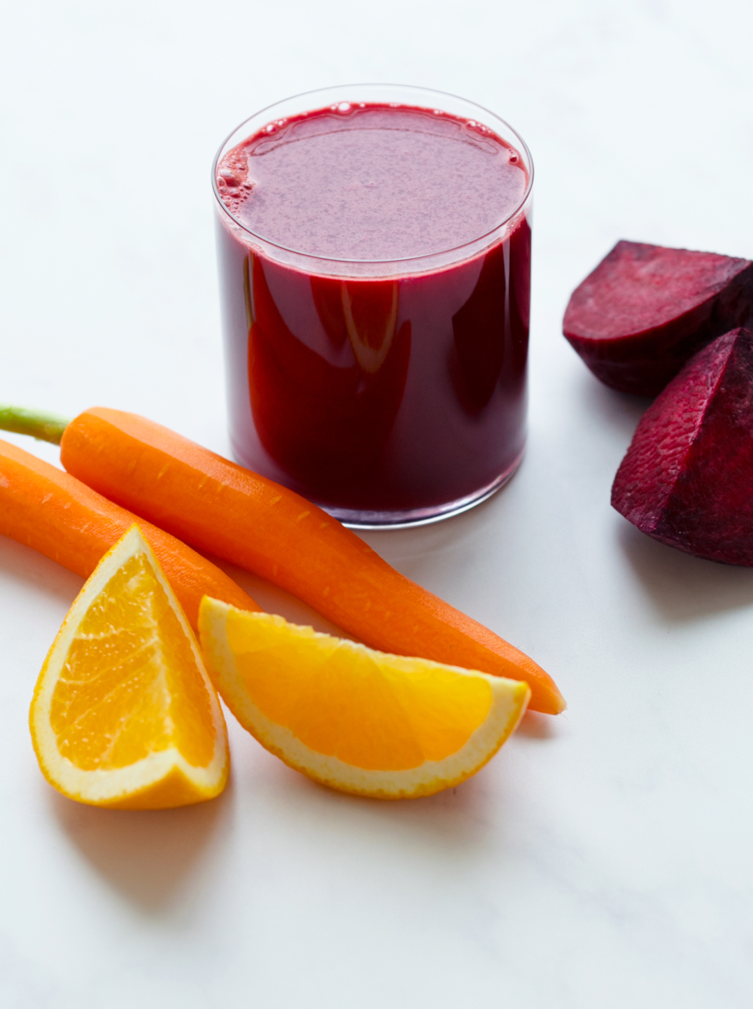 a glass of deep red juice with ingredients beets carrots and orange 
