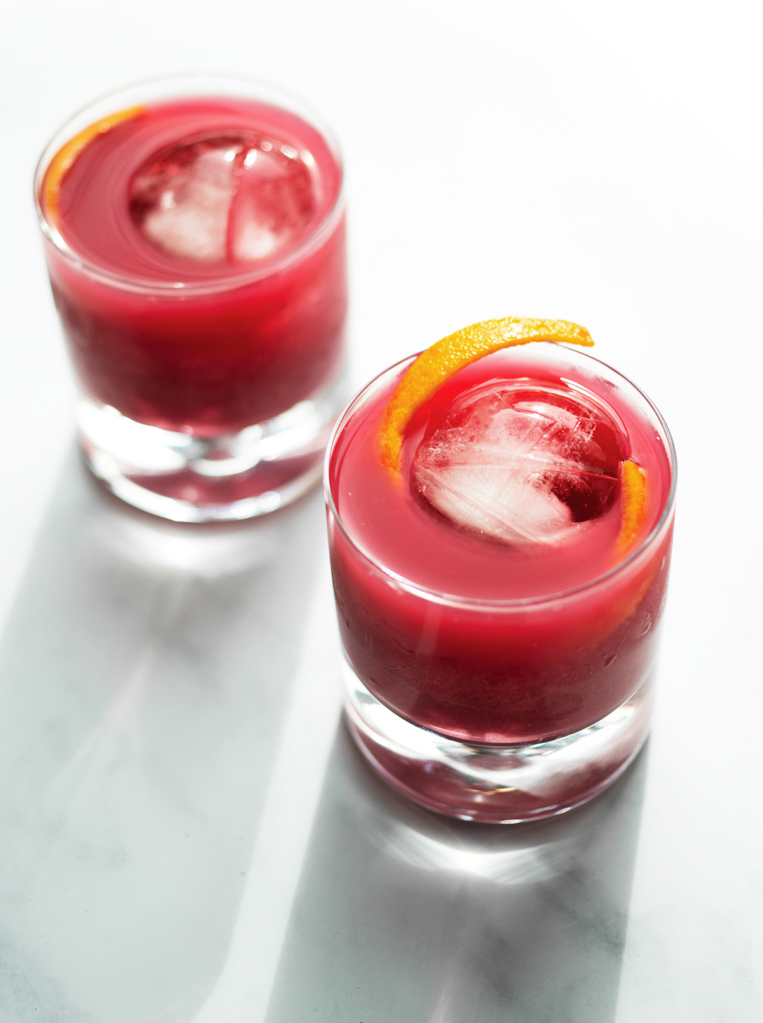 Two No-groni mocktails in glass tumblers with ice and a sliver of orange peel.