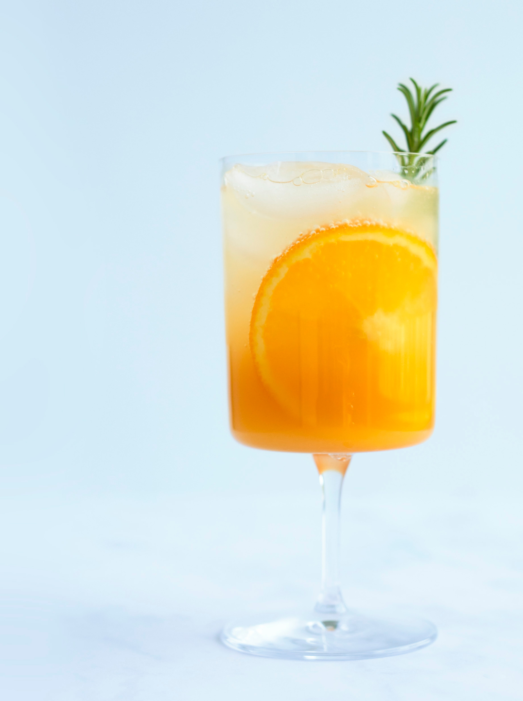 Glass filled with Aperoless Spritz a slice or orange and a sprig of rosemary