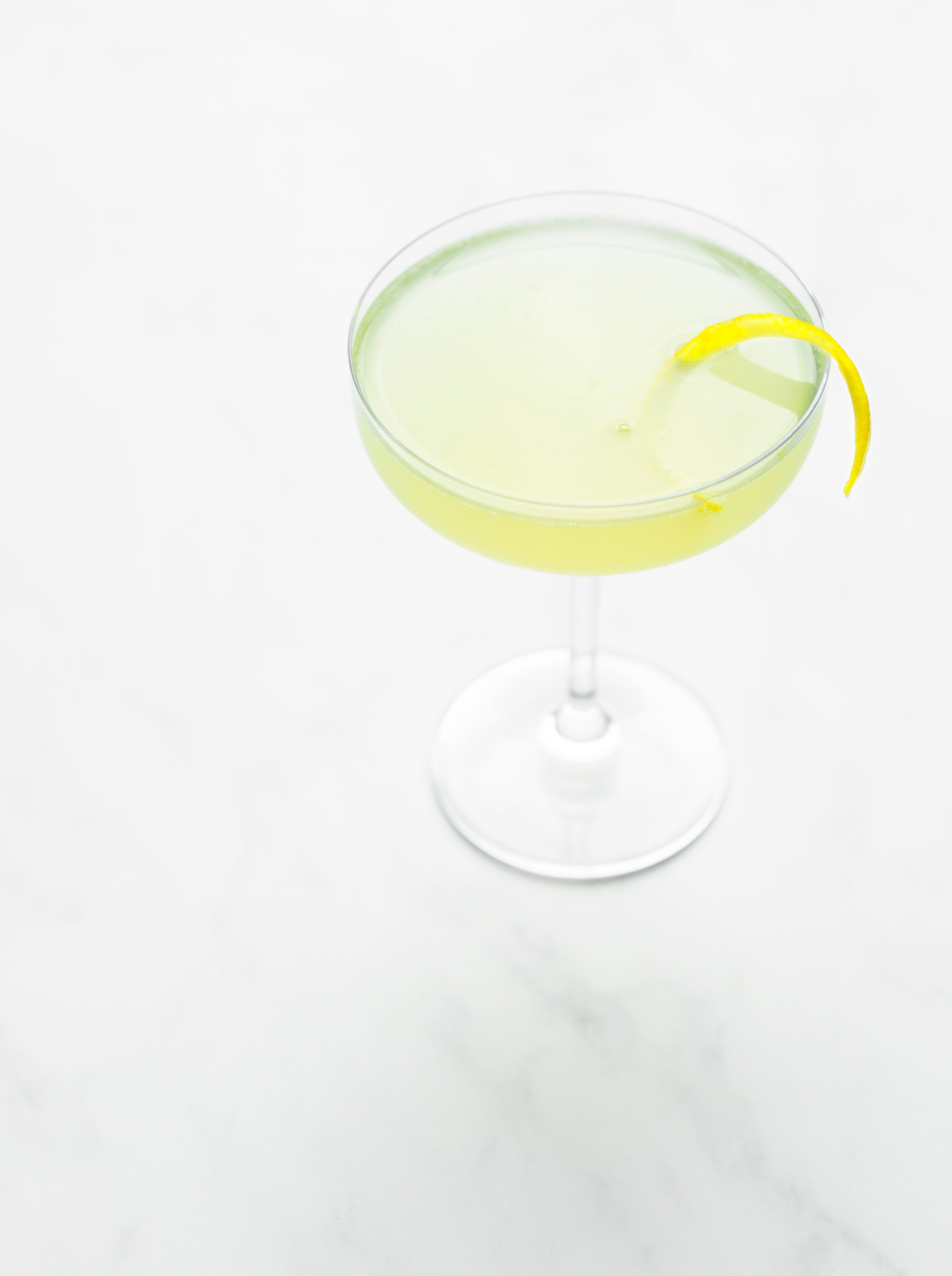 A martini glass filled lemon green juice garnished a sliver of lemon peel