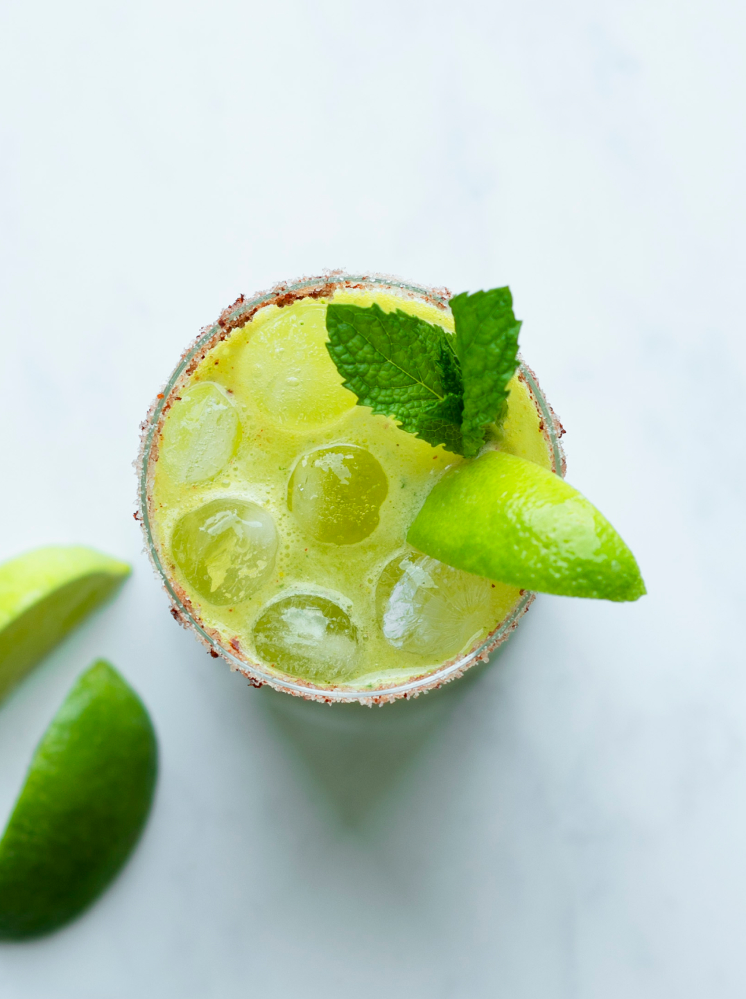 A green juice mocktail topped with lime segments and a sprig of mint