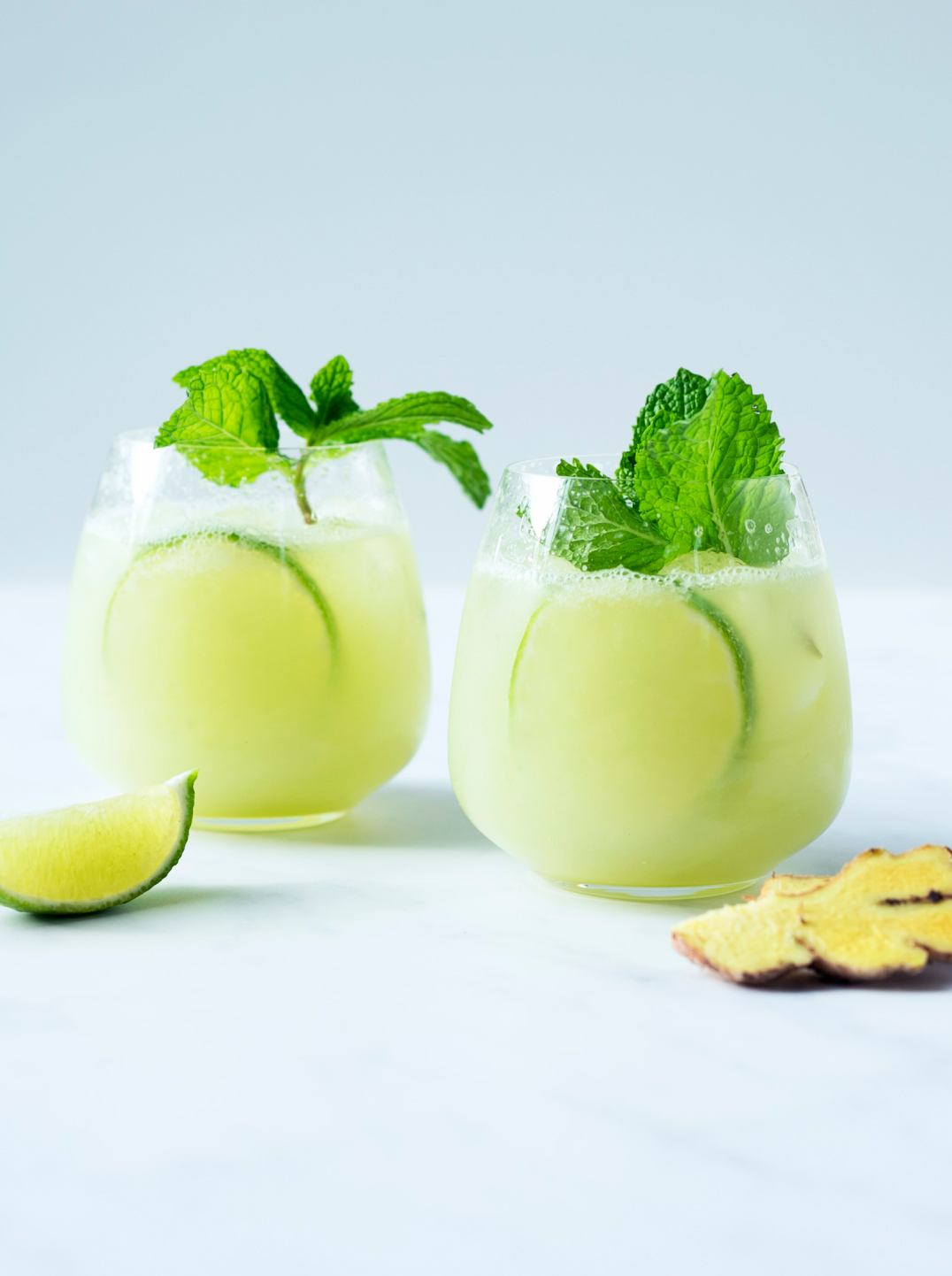 Two glasses filled with a light lime green juice garnished with lime slices and mint