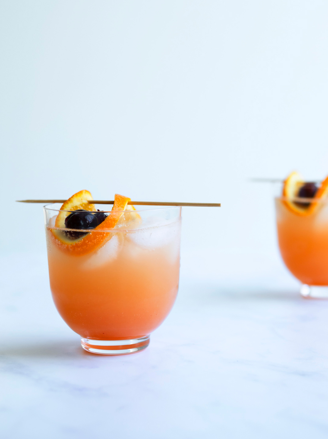 A glass filled with a orange juice and ice garnished with orange peel on a skewer