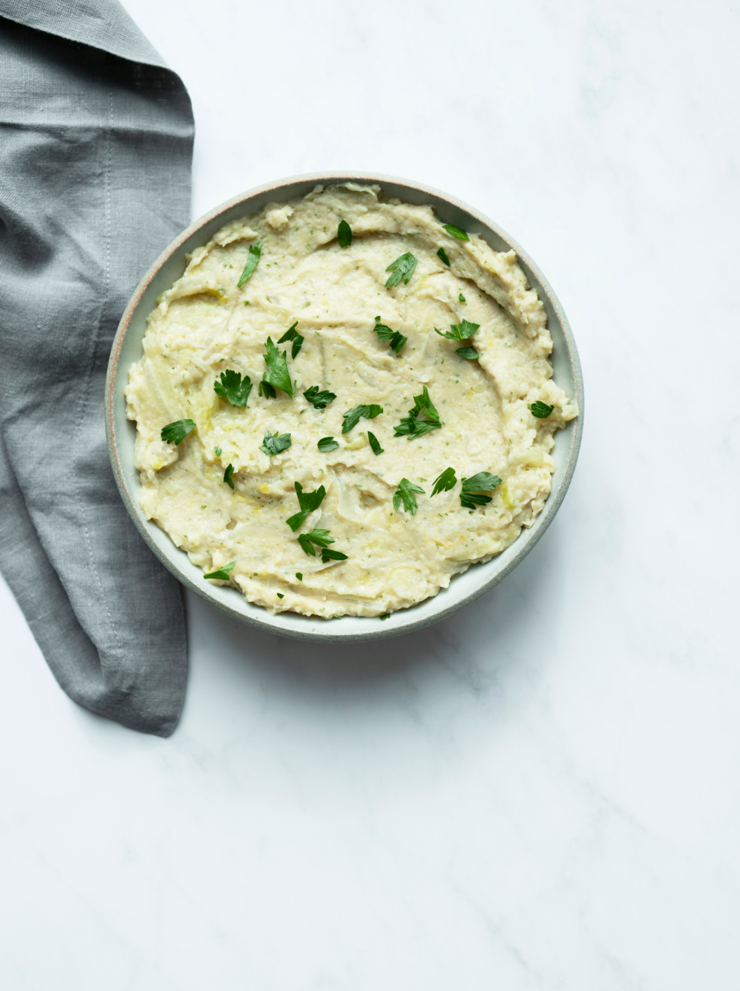 A ceramic bowl filled with white bean dip with garnished with parsley