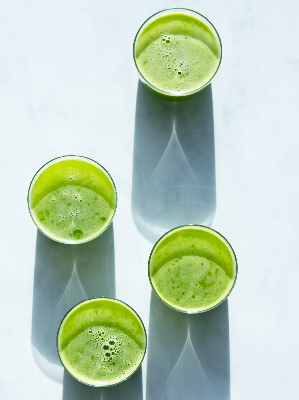 Overhead view of 5 tall glasses filled with Spicy Green Garland juice on a pale blue background. 