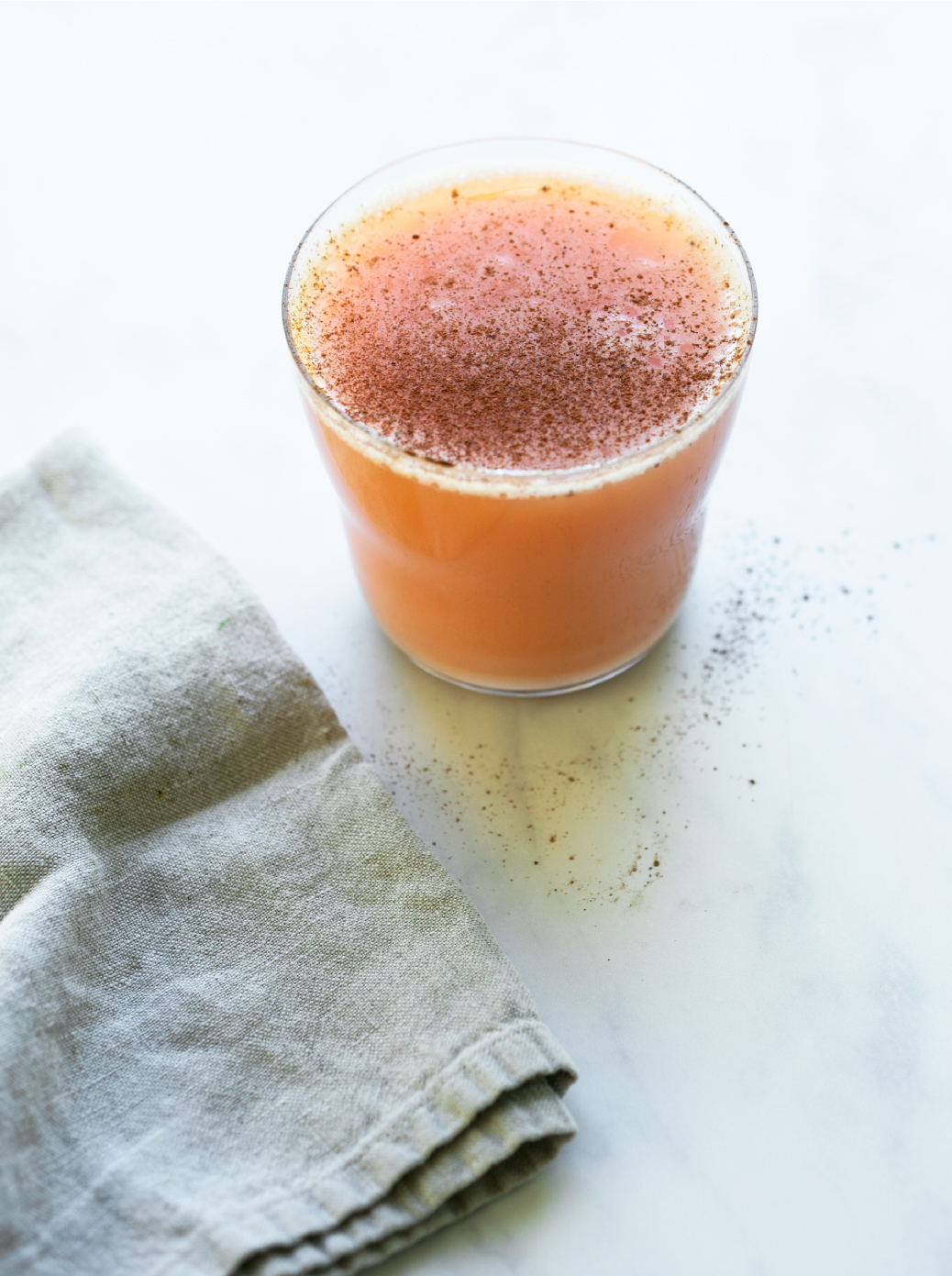 A glass filled with Sweet Potato Spice Juice on a marble counter with a gray linen napkin in the bottom left corner. 