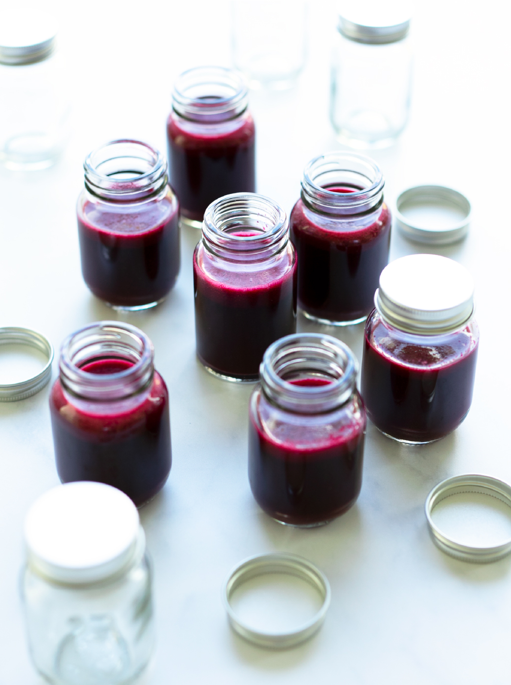 A group of small glass bottles filled with Beet-Cranberry Booster shots