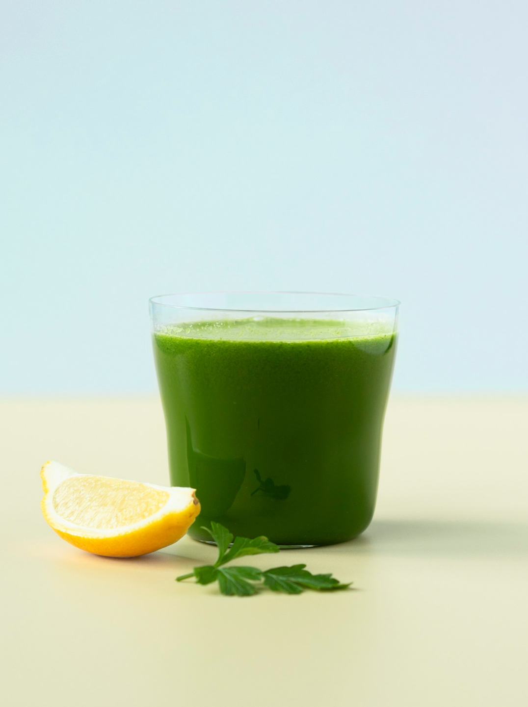 glass of dark green juice with a piece of lemon and sprig of parsley 
