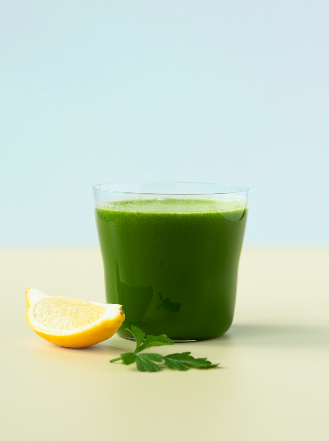 glass of dark green juice with a piece of lemon and sprig of parsley