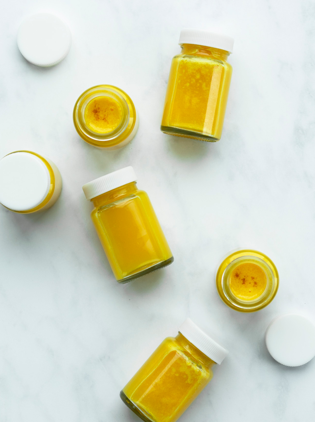 6 small bottle filled with deep yellow immune builder shots on a marble background