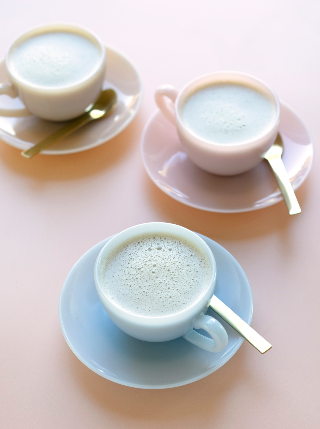 3 pastel colored tea cups filled with dandelion
 chai on pale pink background
